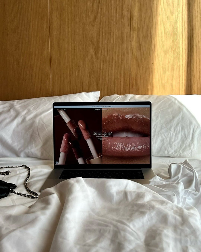 Laptop on a bed displaying a makeup product with a wooden headboard in the background