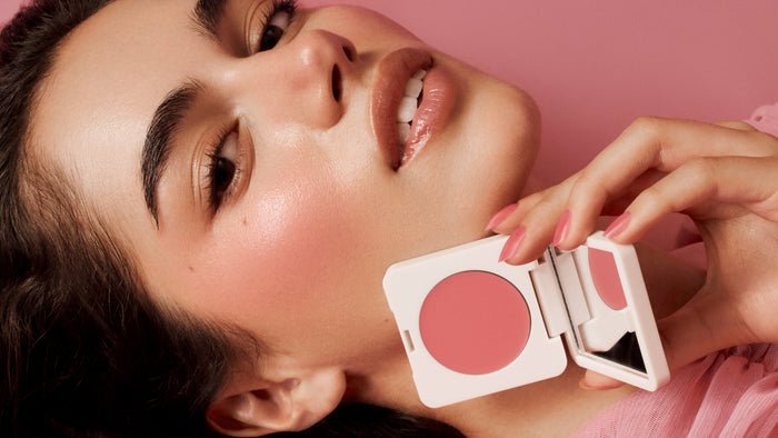 Close-up of a woman applying blush to her face with a compact mirror.