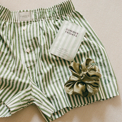 Green and white striped shorts with a hair scrunchie and 'Summer Fridays' product on a textured surface