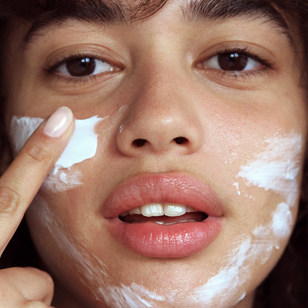 Close-up of a woman applying Jet Lag Mask to her face with her finger.