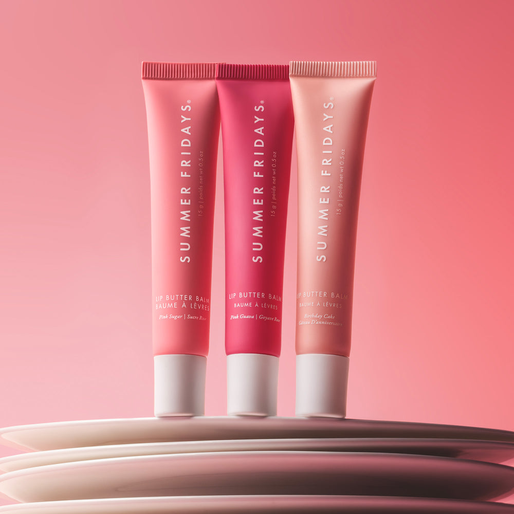 Three 'Summer Fridays' lip butter tubes on a pink background