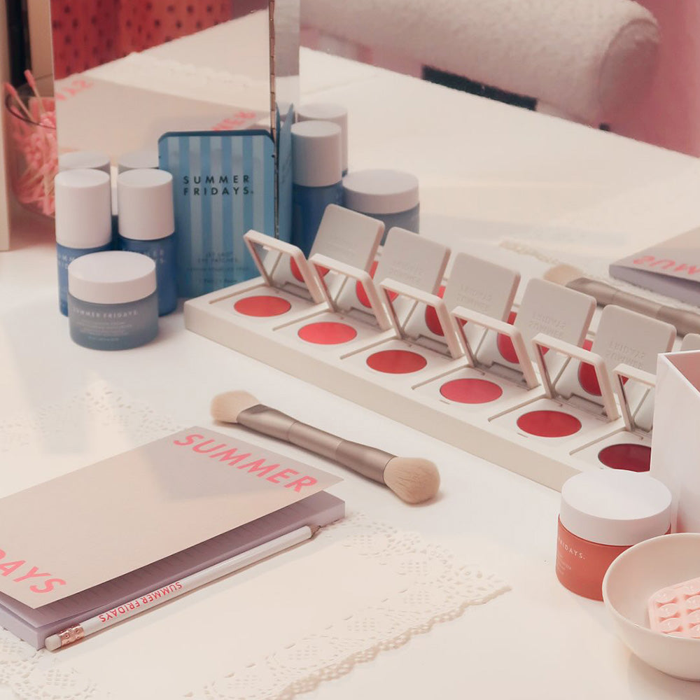 Makeup products including a palette, jars, and a brush on a white surface with 'Summer Fridays' branding.