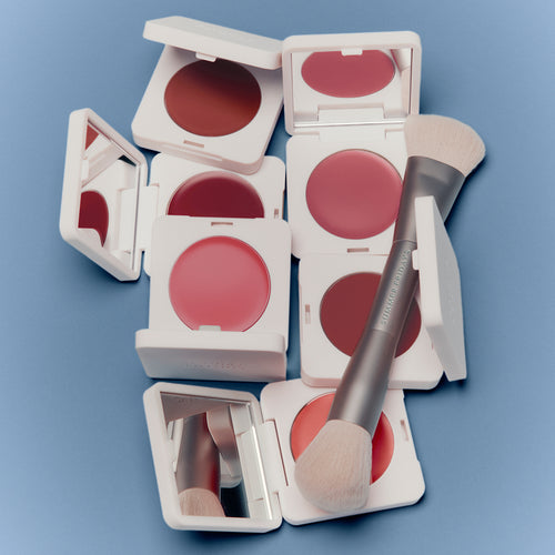 Multiple open blush compact cases with pink blush and a brush on a blue background