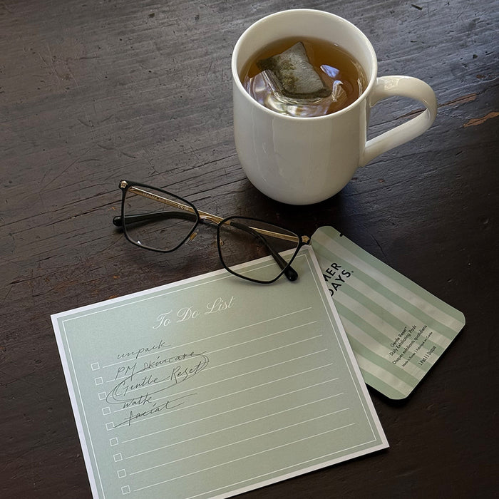 White mug with tea, glasses, and a notepad on a wooden surface