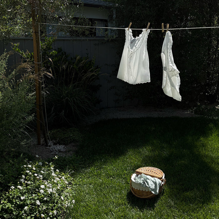 White shirts hanging on a clothesline in a garden with a basket of laundry on the grass.