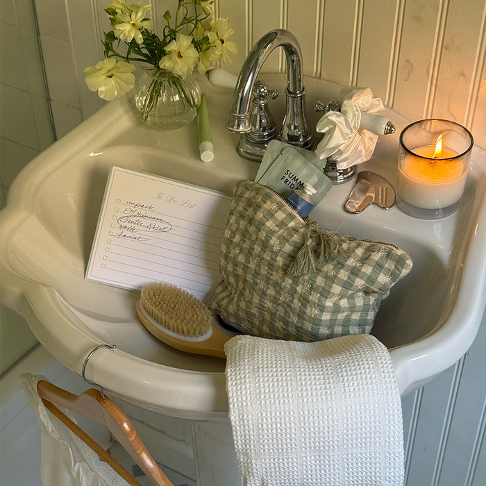 Bathroom sink with toiletries, a candle, and a letter on a checkered towel.