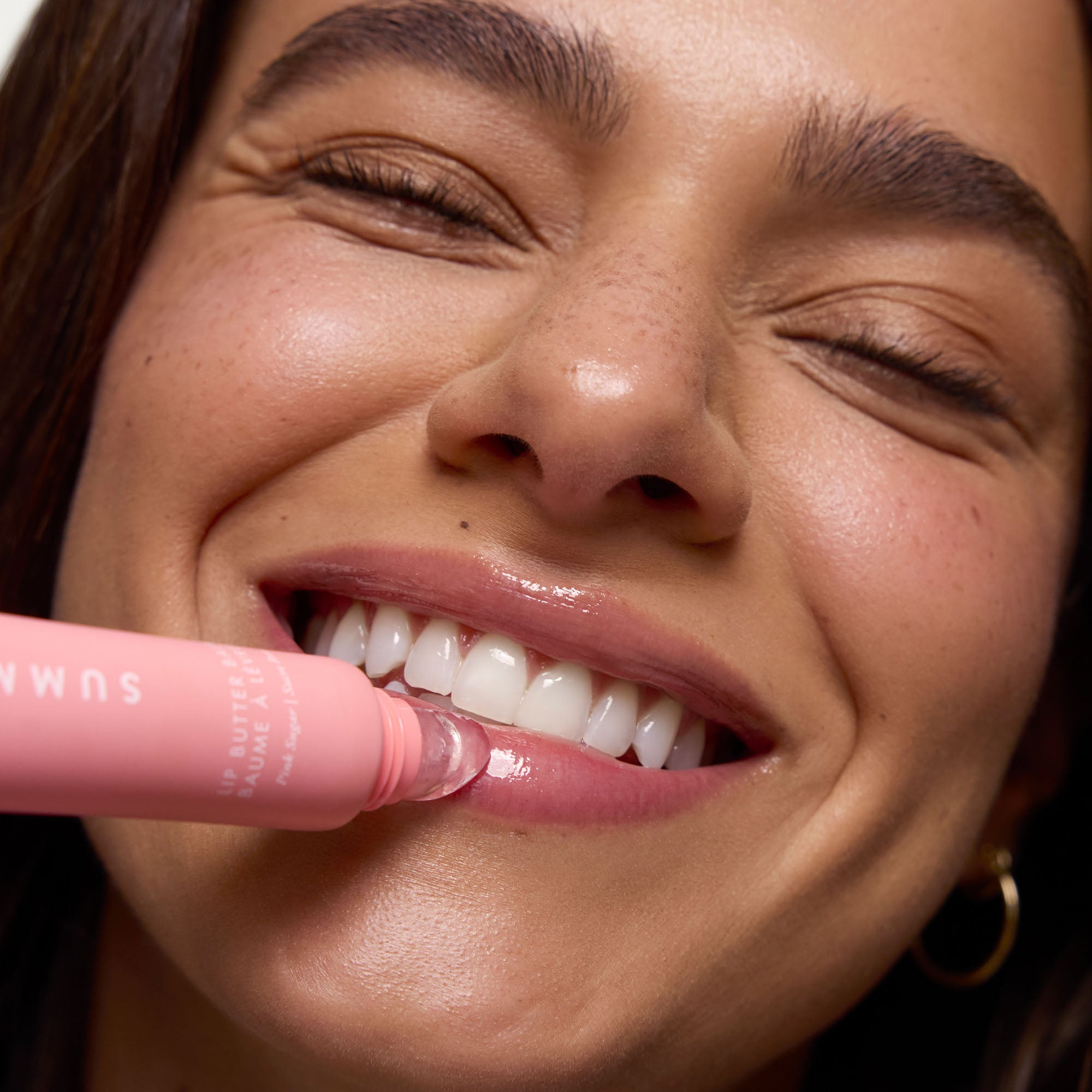 Close-up of a woman applying pink lipstick with a focus on her lips and the product.