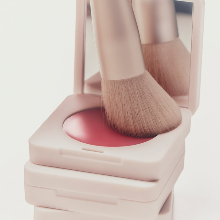 Makeup brush on a pink compact case with a blurred background