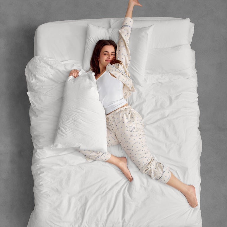 Woman lying on a large bed with white bedding and pillows.