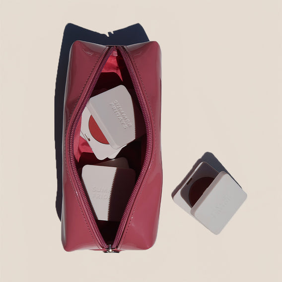 Pink toiletry bag with a mirror and travel items on a beige background