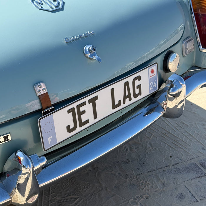 Car with a license plate reading 'JET LAG' on a light blue background