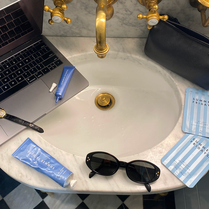 Marble sink with sunglasses, Jet Lag Eye Patches, Jet Lag Mask, Jet Lag Overnight Eye Serum and a laptop resting over it